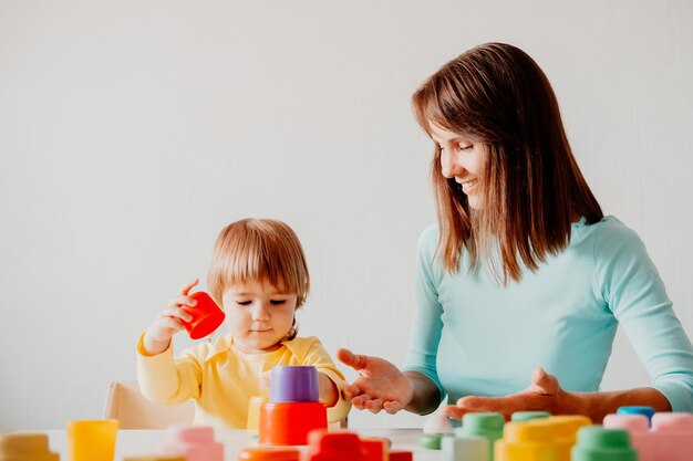 写真 若い女性が小さな娘と遊んでいる白人の女性と子供がテーブルに座って遊んでいる