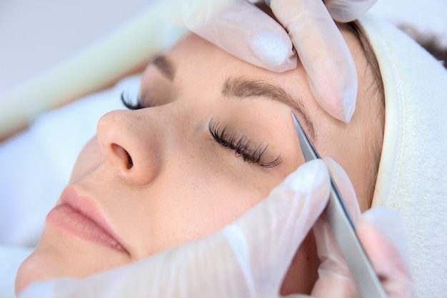 Young woman plucking eyebrows with tweezers close up.