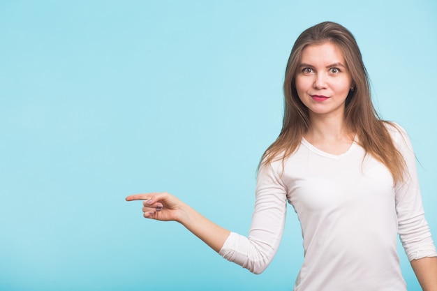 Young woman pointing at copy space on blue background