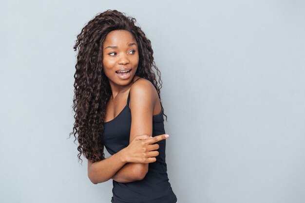 Young woman pointing finger away over gray wall