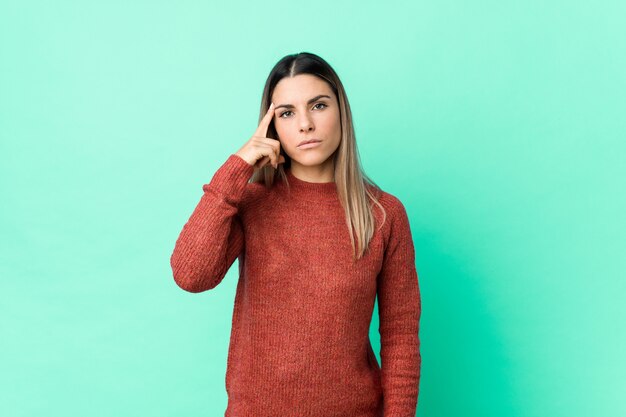 Young woman pointing temple with finger, thinking, focused on a task