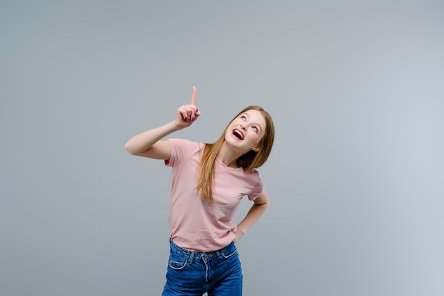 Foto giovane donna che indica in su allo spazio della copia isolato sopra priorità bassa grigia