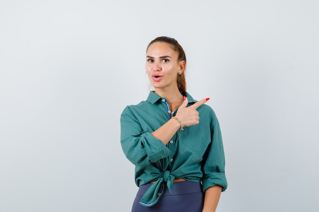 young woman pointing at upper right corner in green shirt and looking wondered. front view.