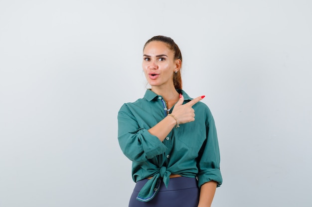 Young woman pointing at upper right corner in green shirt and looking wondered. front view.