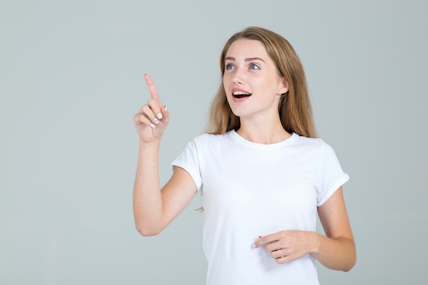 Foto la giovane donna indica un dito al lato e su, isolato su gray