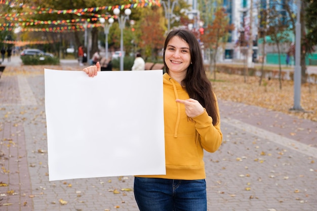 A young woman points her finger at a blank sheet of paper and smiles