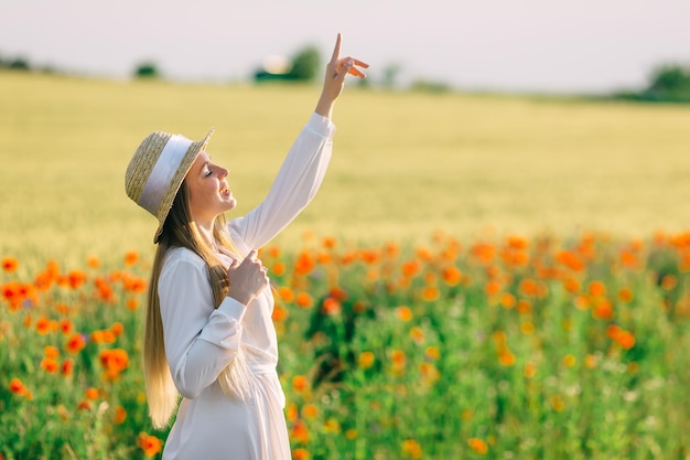 Young woman on poppy field girl raised her hand and showing finger white dress and boater
