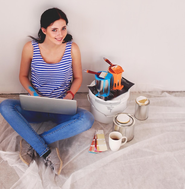 Ritratto di giovane donna durante la pittura nuovo appartamento seduto con il computer portatile giovane donna con il computer portatile