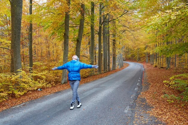 道路上の秋の森でポーズをとって若い女性