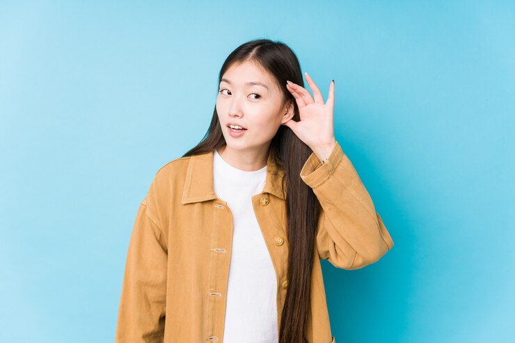 Photo 若い女性がゴシップを聴こうとして分離された青い壁でポーズ