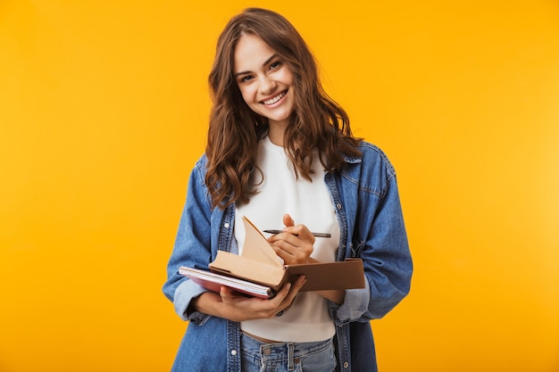 Young woman posing isolated over yellow wall reading book take notes.