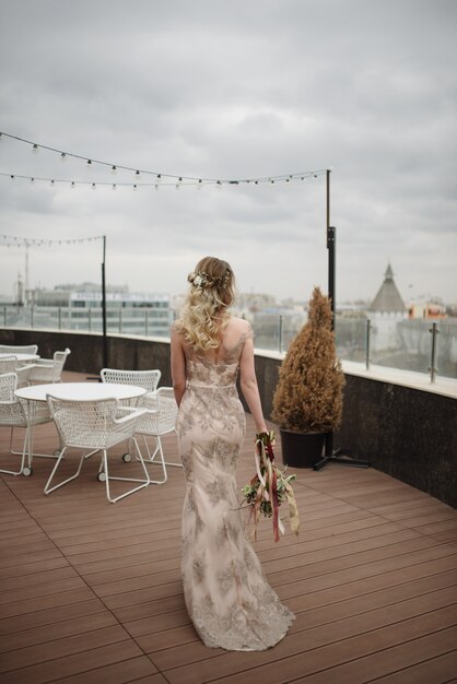 Young woman posing in a light long lace dress with a bouquet of flowers in her hands