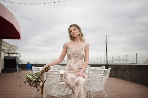 Young woman posing in a light long lace dress with a bouquet of flowers in her hands