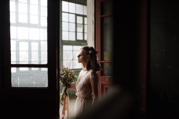 Young woman posing in a pink long dress backs indoors