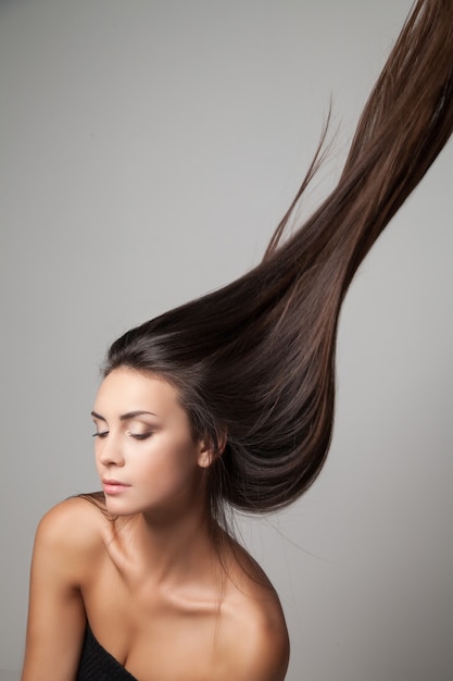 Young woman posing with her long hair thrown up. Vertical studio shot.