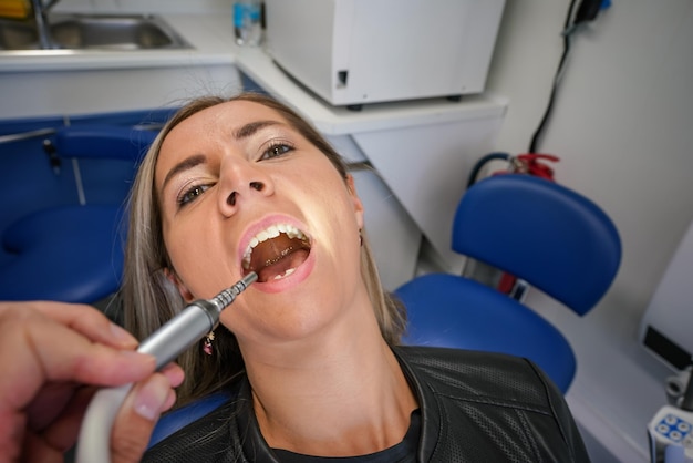 Foto giovane donna che posa con la bocca aperta alla sedia del dentista strumento dentale vicino ai suoi denti vista in prima persona