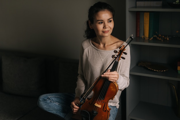 Young woman posing with a violin at home sitting on the couch. Girl is posing with musical instrument.