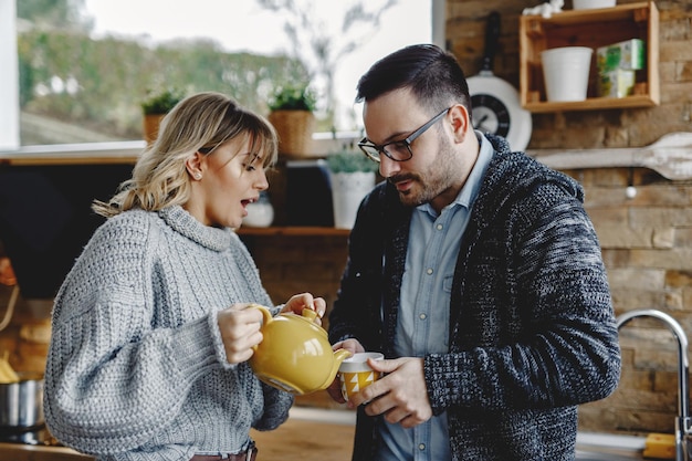 Young woman pouring tea to her husband while standing in the kitchen