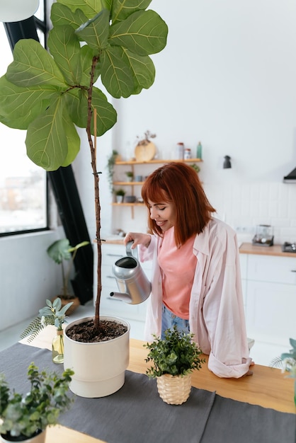 Young woman pouring water in flower pot with indoor houseplant from watering can