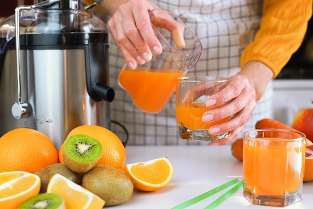 young woman pours freshly fresh fruit juice into a glass making healthy fruit juices at home