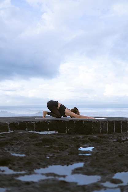 若い女性は日の出の美しいビーチでヨガを練習します。青い空、海、波、自然への近さ、自然との一体感。