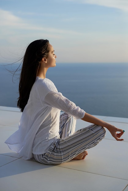 молодая женщина практикует медитацию йоги на закате с видом на океан на заднем плане