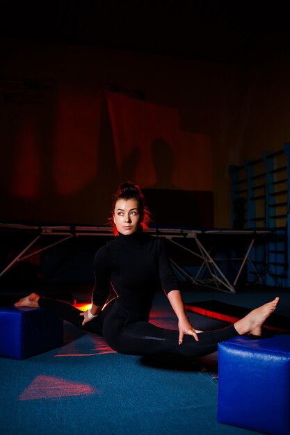 Young woman practices twine sitting. Athletic girl doing gymnastics in the gym. Active lifestyle