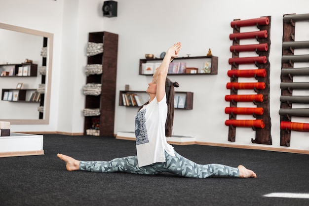 Young woman practices yoga in a fitness room. Professional girl trainer stretches muscles before training indoors.