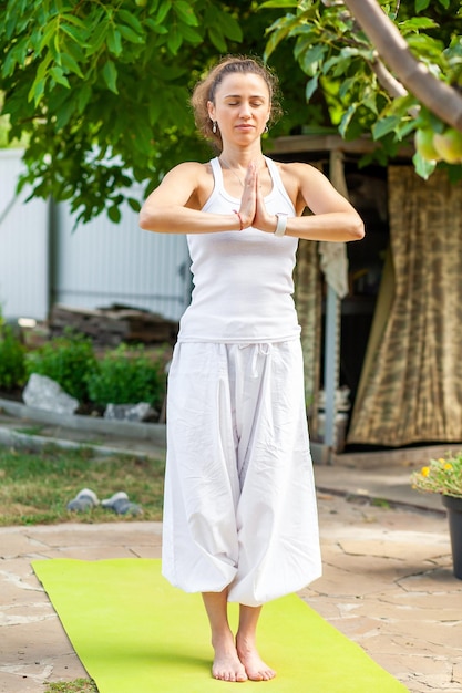 Young woman practices yoga in the summer garden Namaskar Mudra Surya Namaskar Mountain Pose Tadasana