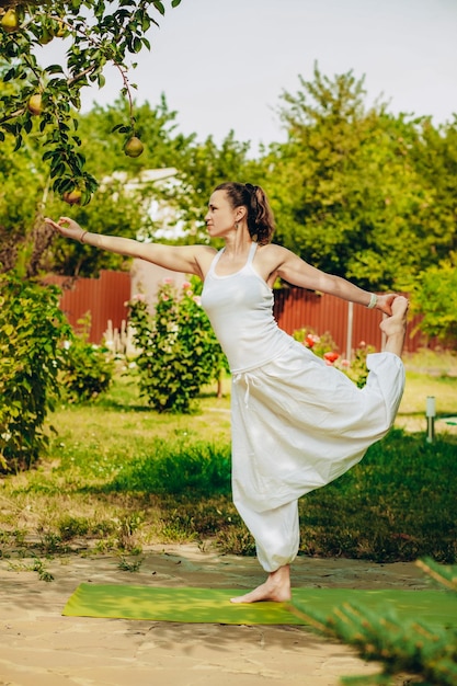 Young woman practices yoga in the summer garden Natarajasana Lord of the Dance Pose or Dancer Pose