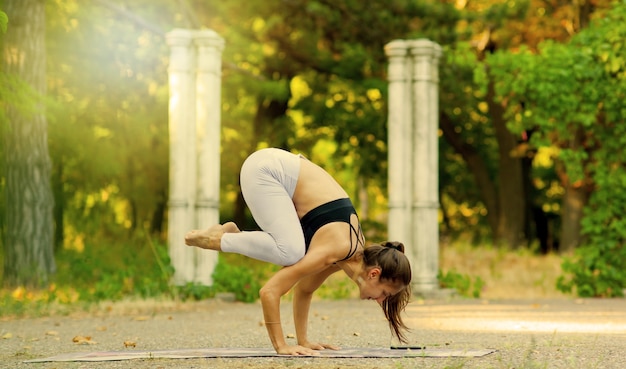 Giovane donna che pratica la posa di yoga d'equilibratura all'aperto