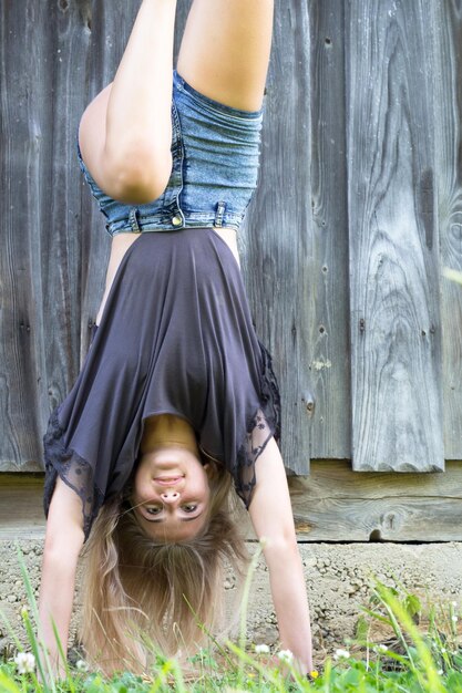 Photo young woman practicing handstand against wooden wall