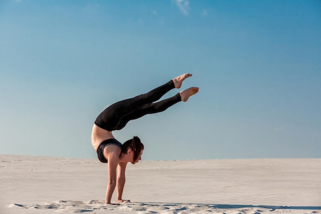 Young woman practicing handstand on beach with white sand and bright blue sky