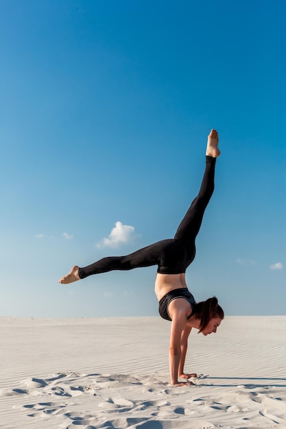 Foto giovane donna che pratica la verticale sulla spiaggia con sabbia bianca e cielo blu brillante