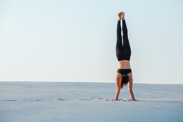 Young woman practicing inversion balancing yoga pose handstand on sand