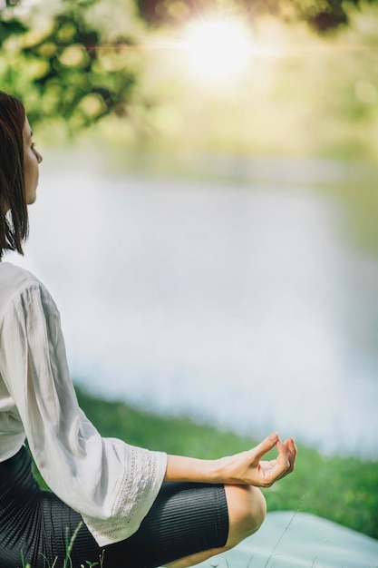 自然の中の水の近くで瞑想を実践する若い女性