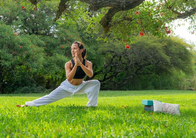 Молодая женщина, практикующая йогу, позирует с боковым выпадом под деревом в парке