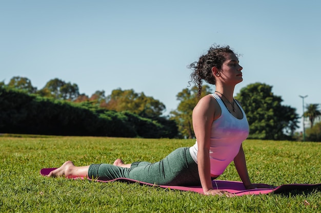 Young woman practicing yoga doing cobra pose in a park