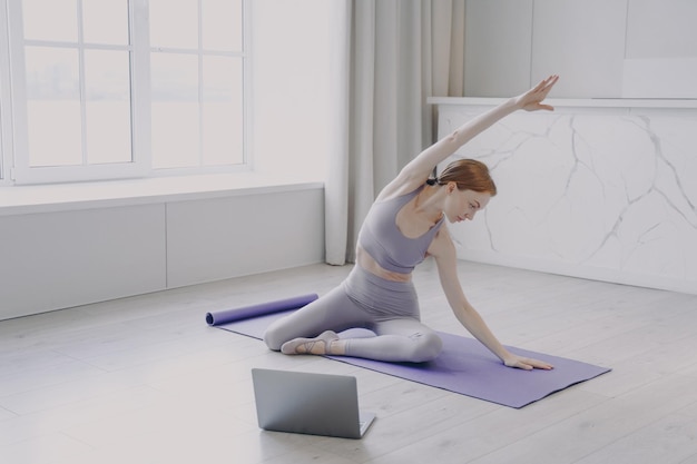 Giovane donna che pratica yoga sul tappetino da ginnastica sport femminili e lezioni online a casa in quarantena