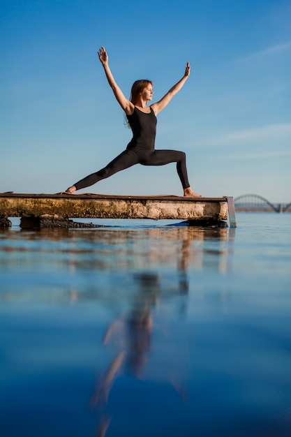 Young woman practicing yoga exercise at quiet wooden pier 