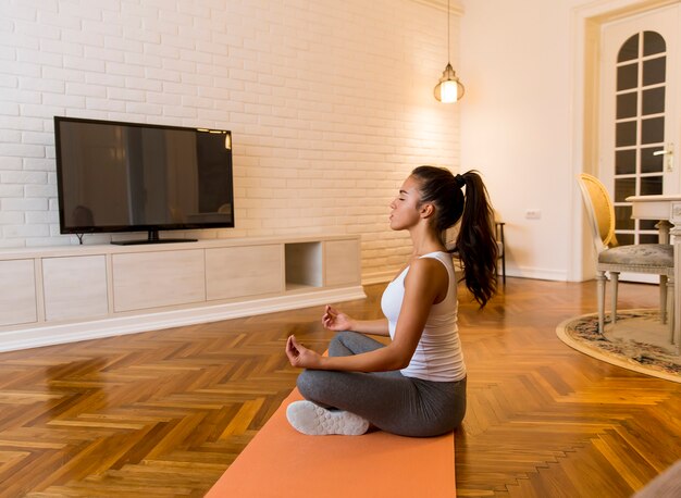 Young woman practicing yoga lotus position in apartment
