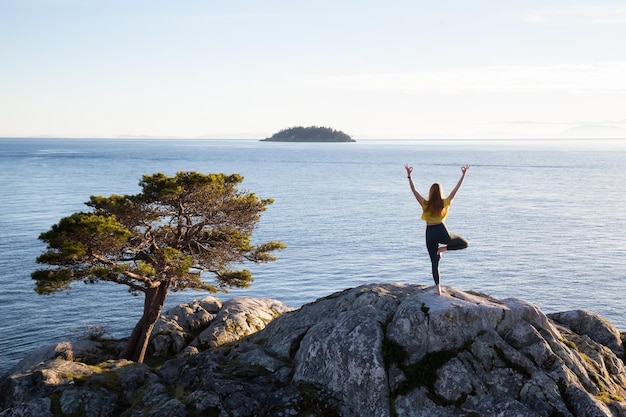 Young woman practicing yoga on a rocky island during a vibrant sunset