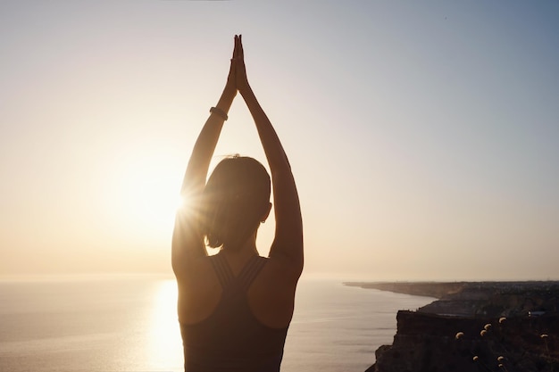 Young woman practicing yoga over sunset sea