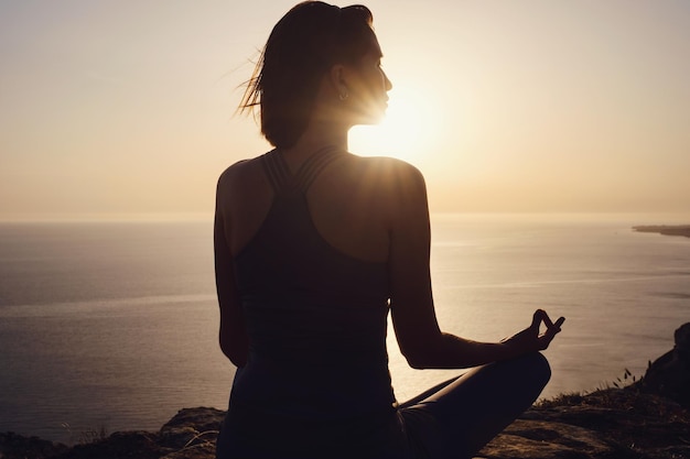 Young woman practicing yoga over sunset sea