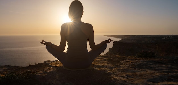 Giovane donna che pratica yoga sul mare al tramonto