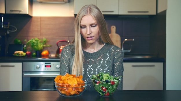 Giovane donna che preferisce l'insalata alle patatine fritte