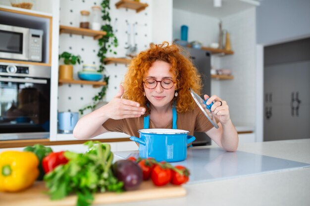 Young woman prepares lunch in her kitchen As she cooks she takes a moment to relish the mouthwatering aroma With excitement she tries out a new recipe preparing a delightful dinner for her family