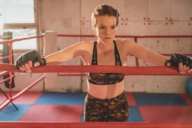 Young woman prepares for matches MMA in the cage. Training in a sport hall