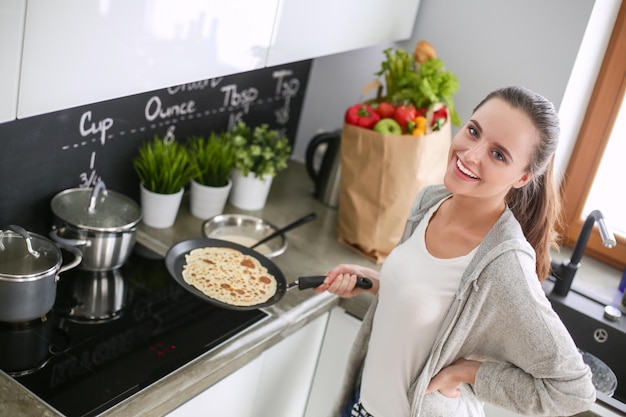 Young woman prepares pancakes in the kitchen while standing near the table Woman in the kitchen Cooking at kitchen