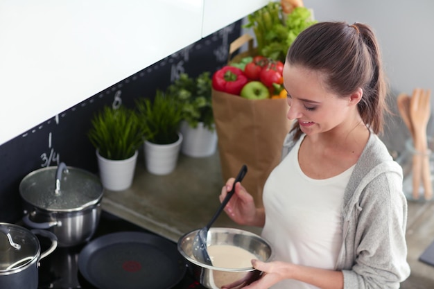 Young woman prepares pancakes in the kitchen while standing near the table Woman in the kitchen Cooking at kitchen